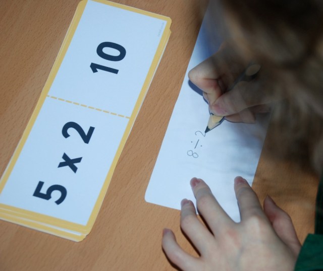 Writing out the division sums on the reverse side of her multiplication cards