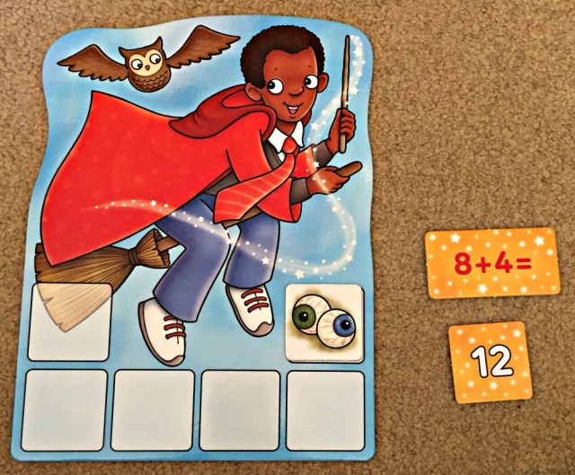 Playing Magic Maths by Orchard toys. Pick a sum card and find the correct answer card to reveal an ingredient to go onto your board